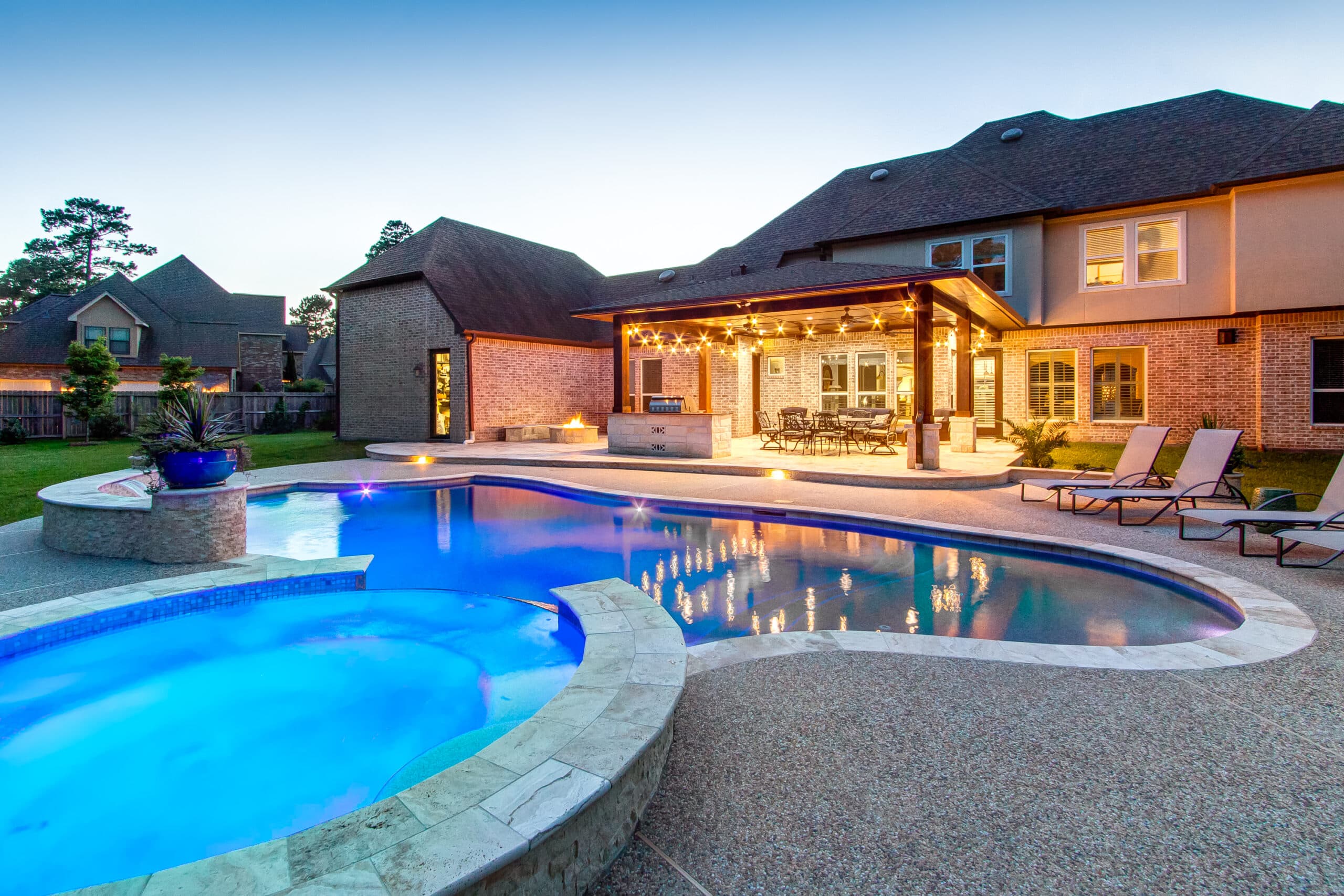 Remodeled Houston backyard with a curved pool, covered patio, outdoor kitchen, and string lights