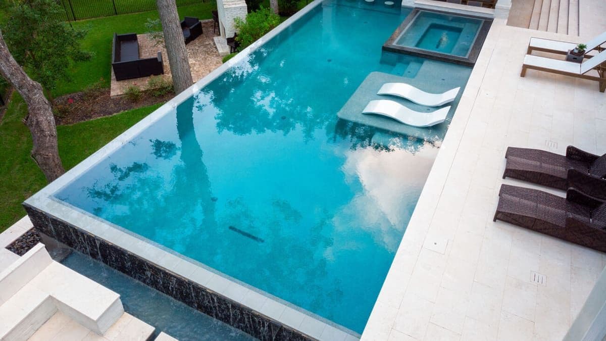 Aerial view of a Houston backyard infinity-edge pool and raised spa framed by patio seating and mature trees