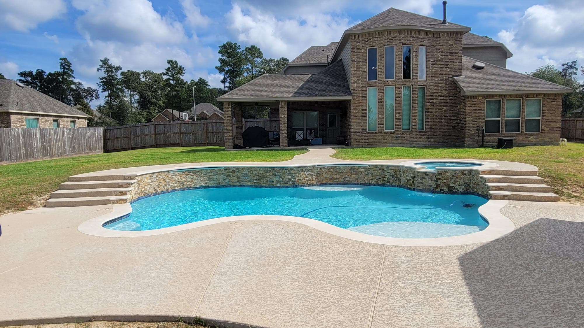 Houston backyard lot with a freeform pool and raised spa in front of a two-story brick home