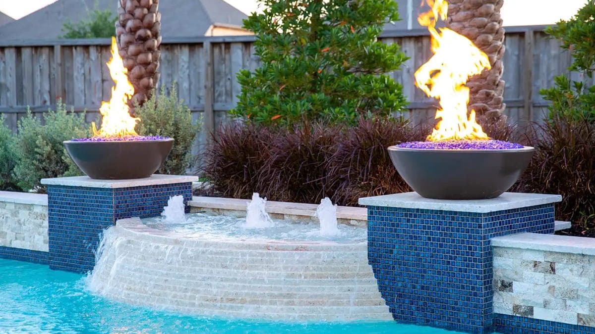 Glowing fire bowls framing a Houston backyard pool at night