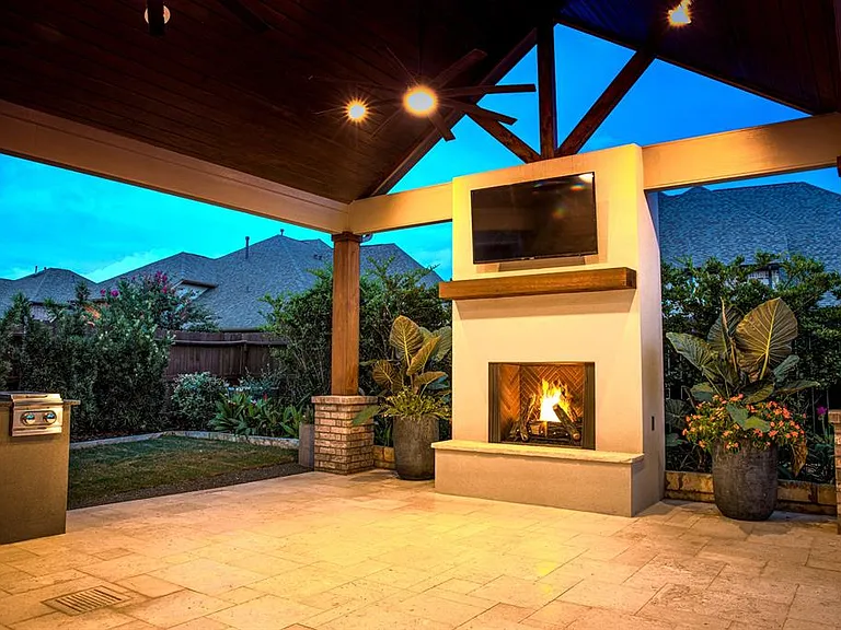Outdoor fireplace by Houston Cool Pools - lit stucco fireplace under a covered patio