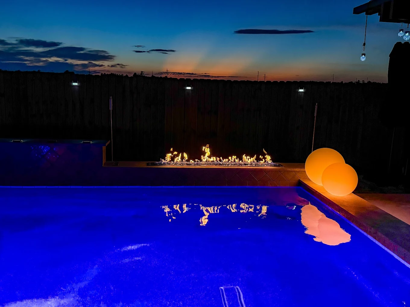 Fire pit by Houston Cool Pools - linear fire feature along the pool wall at dusk